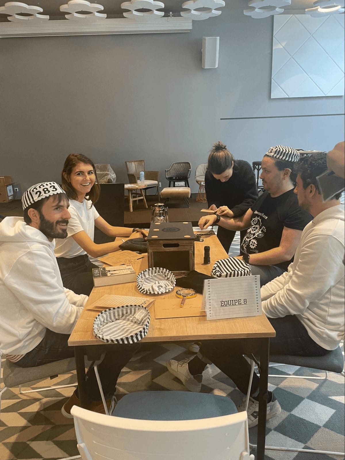 Five Conduktor team members in striped prisoner hats working through an escape-room style puzzle at the offsite