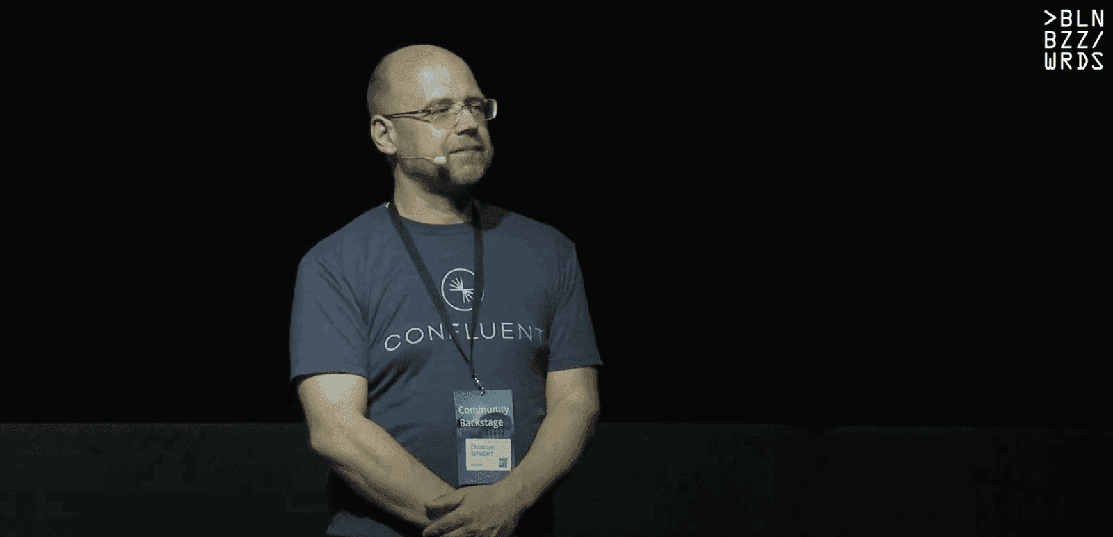 Confluent engineer in branded T-shirt presenting on a darkened conference stage with headset microphone