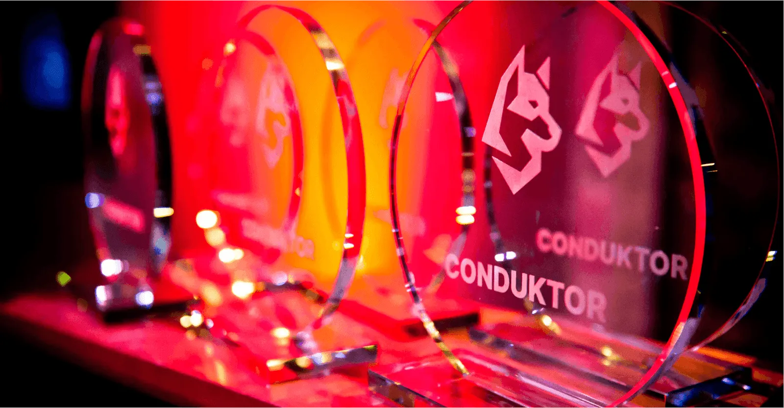 Row of circular glass Conduktor company awards engraved with the wolf logo, lit in red and orange